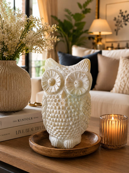 Elegant white owl showpiece on a wooden tray with candle and vase in a cosy living room